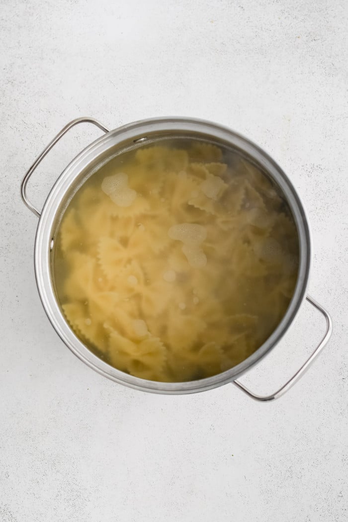 Large pot filled with bowtie shaped pasta cooking in boiling water.