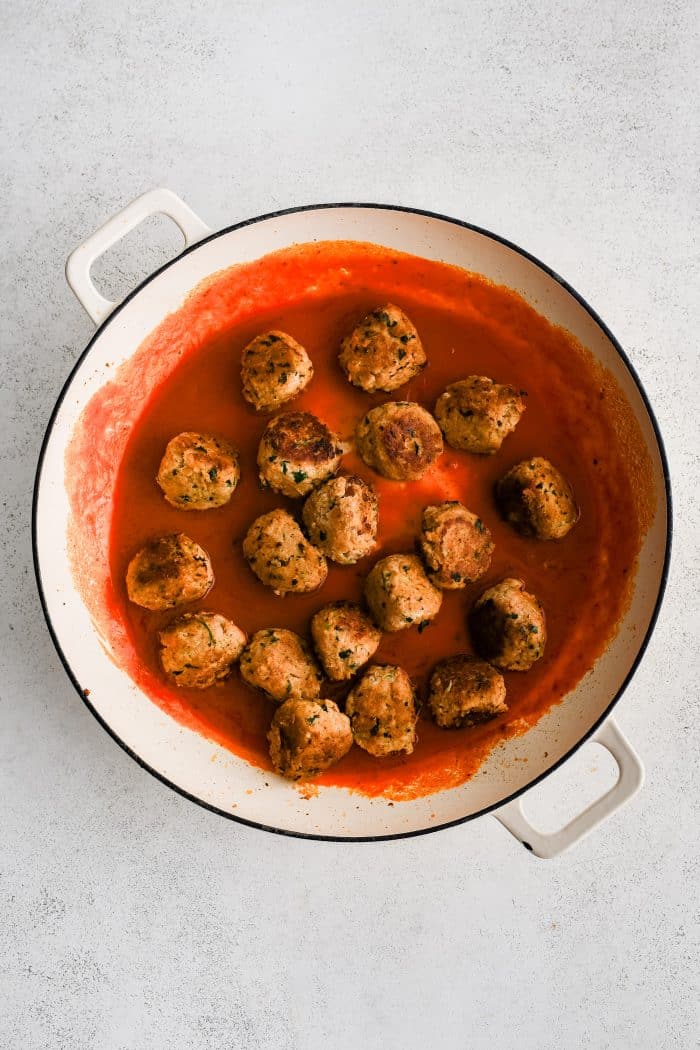 Large skillet filled with pan-fried buffalo chicken meatballs cooking in buttery buffalo sauce.