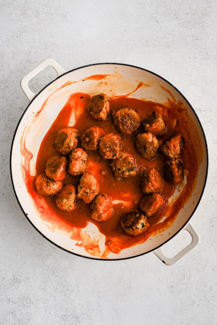 Large skillet filled with pan-fried buffalo chicken meatballs coated in buttery buffalo sauce.