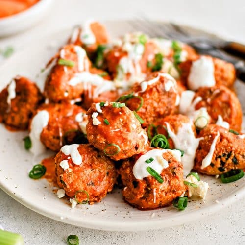 Large speckled serving plate filled with pan-seared buffalo meatballs coated in tangy buffalo sauce, drizzled with ranch dressing, and garnished with sliced green onions.