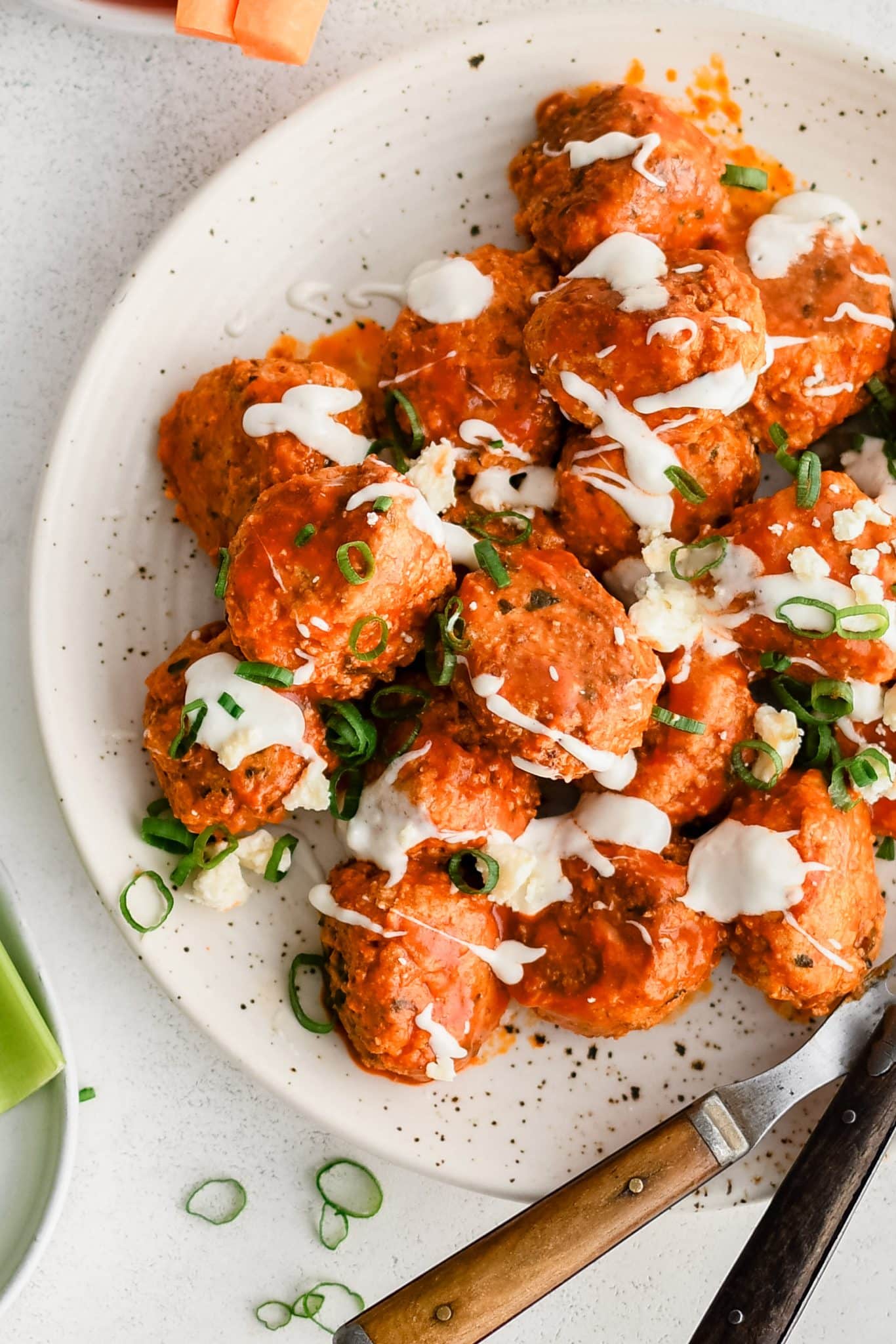 Large speckled serving plate filled with pan-seared buffalo meatballs coated in tangy buffalo sauce, drizzled with ranch dressing, and garnished with sliced green onions.