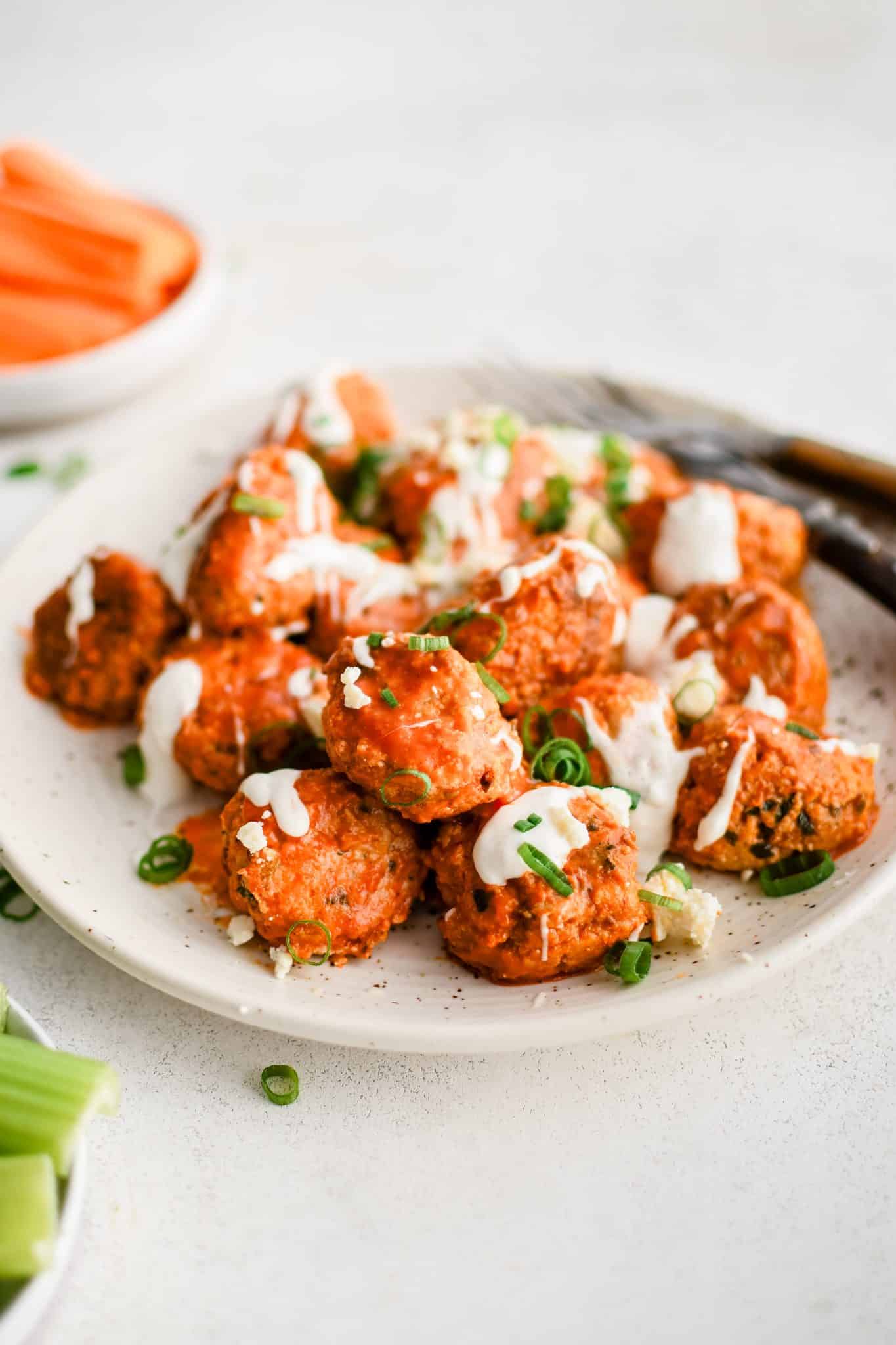 Large speckled serving plate filled with pan-seared buffalo meatballs coated in tangy buffalo sauce, drizzled with ranch dressing, and garnished with sliced green onions.