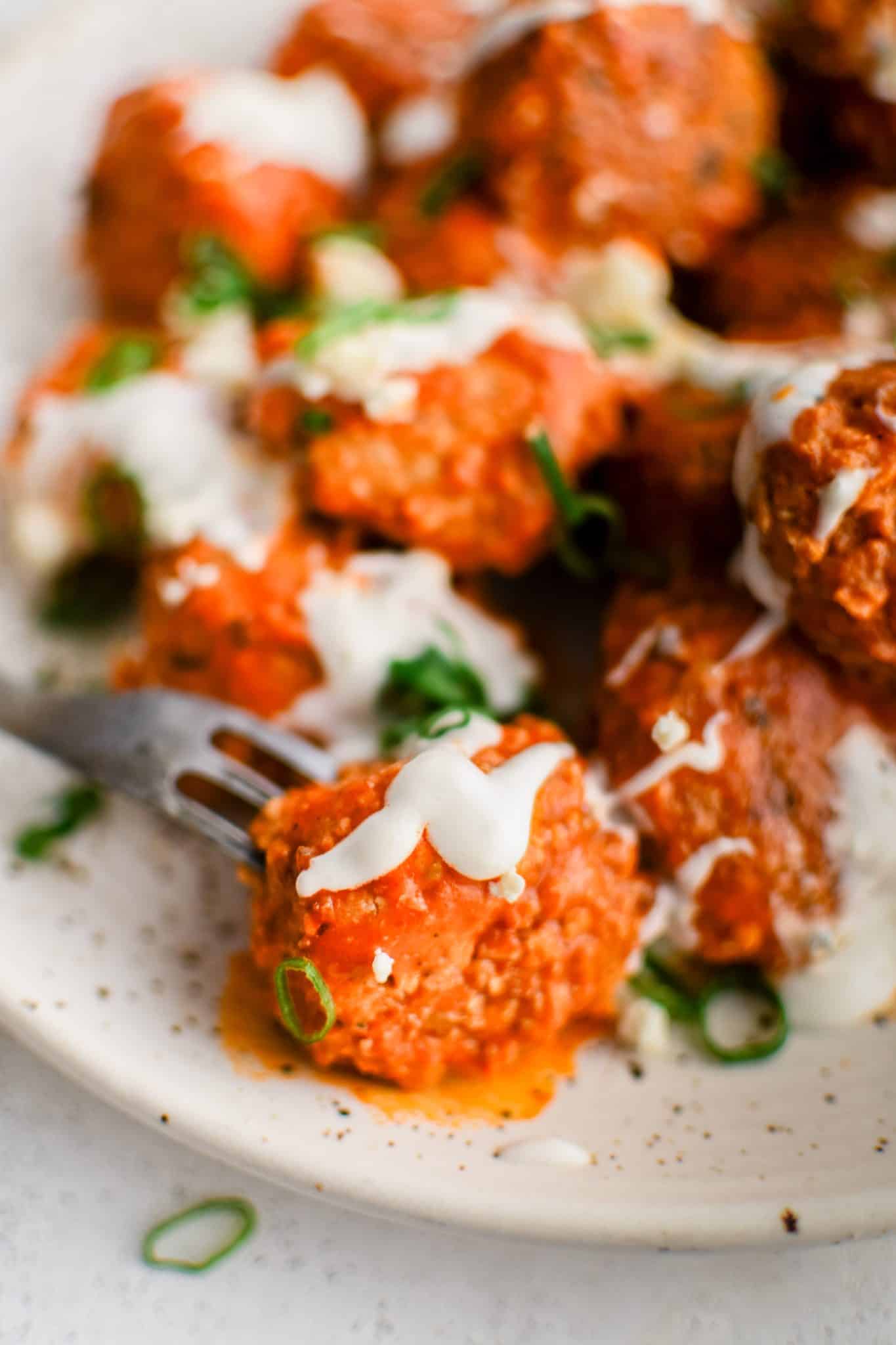 Large speckled serving plate filled with pan-seared buffalo meatballs coated in tangy buffalo sauce, drizzled with ranch dressing, and garnished with sliced green onions.