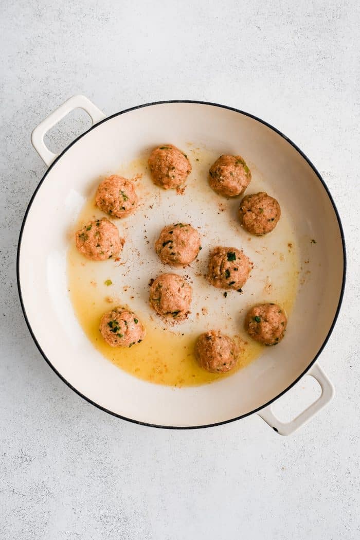 Large skillet filled with eleven buffalo chicken meatballs pan-frying oven medium heat.