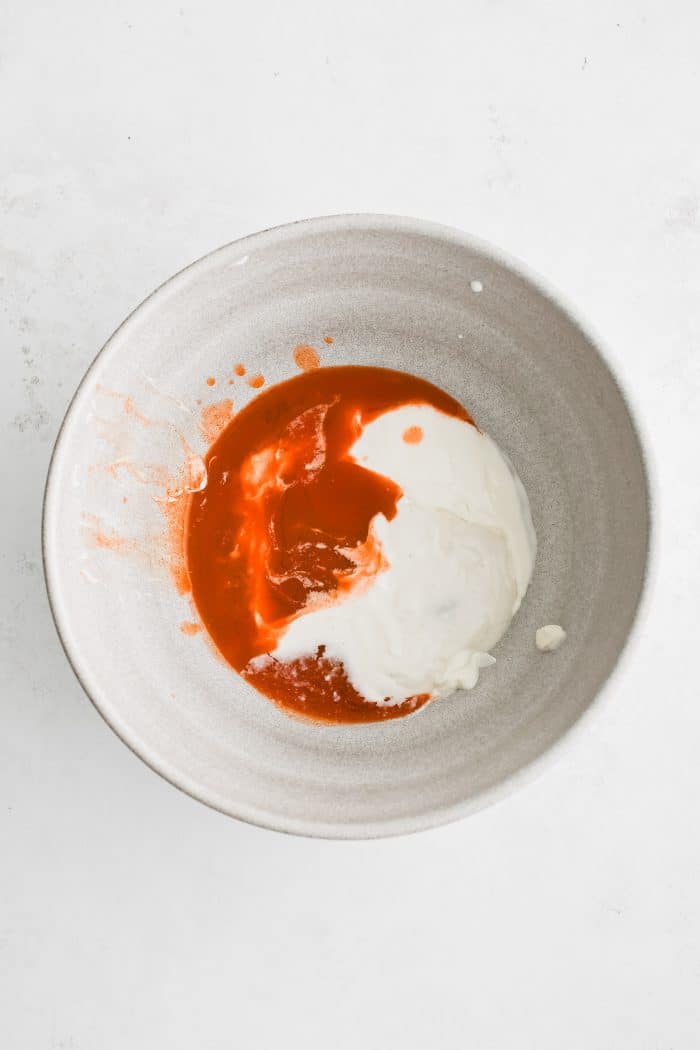 Medium white mixing bowl filled with buffalo sauce, sour cream, and blue cheese dressing.