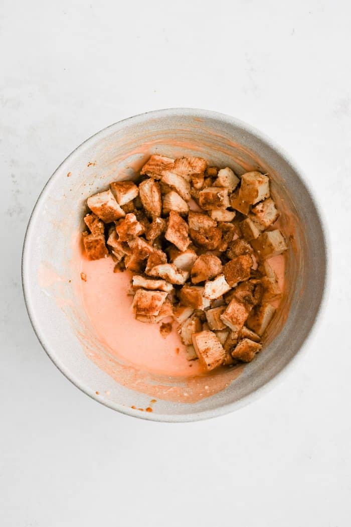 CHopped chicken breast pieces added to large mixing bowl filled with whisked together sauce made from buffalo sauce, sour cream, and blue cheese dressing.