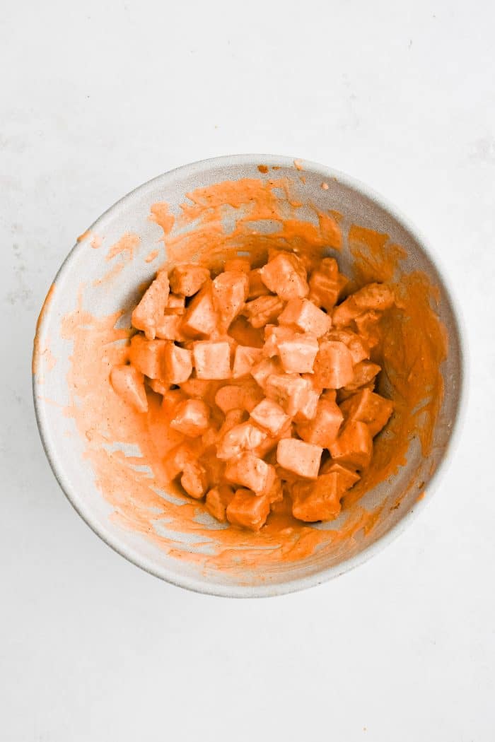 Large white mixing bowl filled with chopped chicken coated in creamy blue cheese and buffalo sauce dressing.