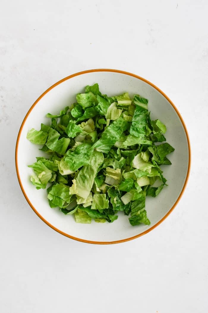 Large white salad bowl filled with fresh chopped Romaine lettuce.