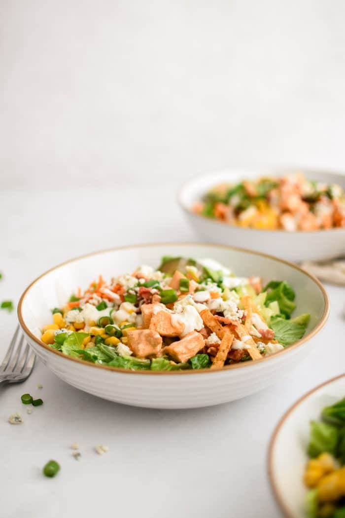 Assembled buffalo chicken chopped salad made with Romaine lettuce topped with creamy buffalo sauce coated chicken, avocado, corn, carrots, celery, green onions, blue cheese, tortilla strips, cooked bacon, and drizzled with creamy ranch dressing.