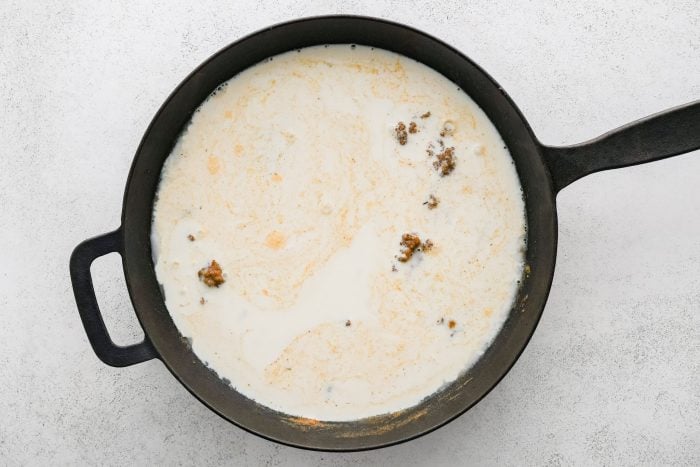 Cast iron skillet filled with heavy cream added to Cajun-spiced roux.