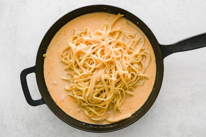 Al dente fettuccine pasta added to simmering Cajun Alfredo sauce.