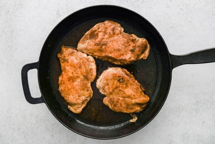 Three pan seared and cooked chicken cutlets in a large cast iron skillet.
