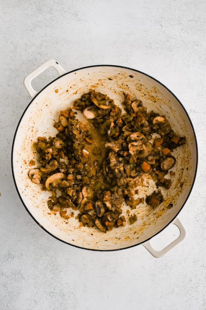 Combination of sauteed onions, carrots, celery, and mushrooms coated in seasoning and all-purpose flour cooking in a large skillet.