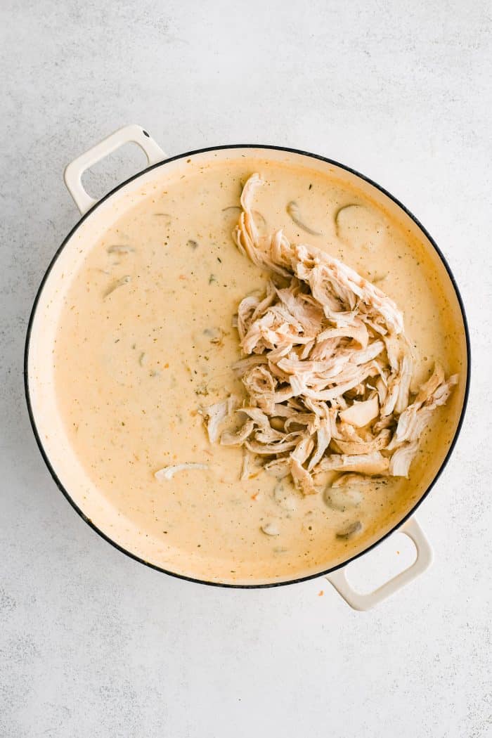 Shredded chicken added to a homemade cheesy, creamy sauce simmering in a large round skillet.