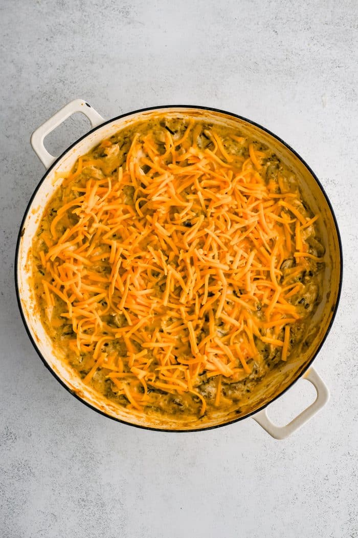 Freshly shredded cheddar cheese sprinkled over a partially baked chicken and wild rice casserole.