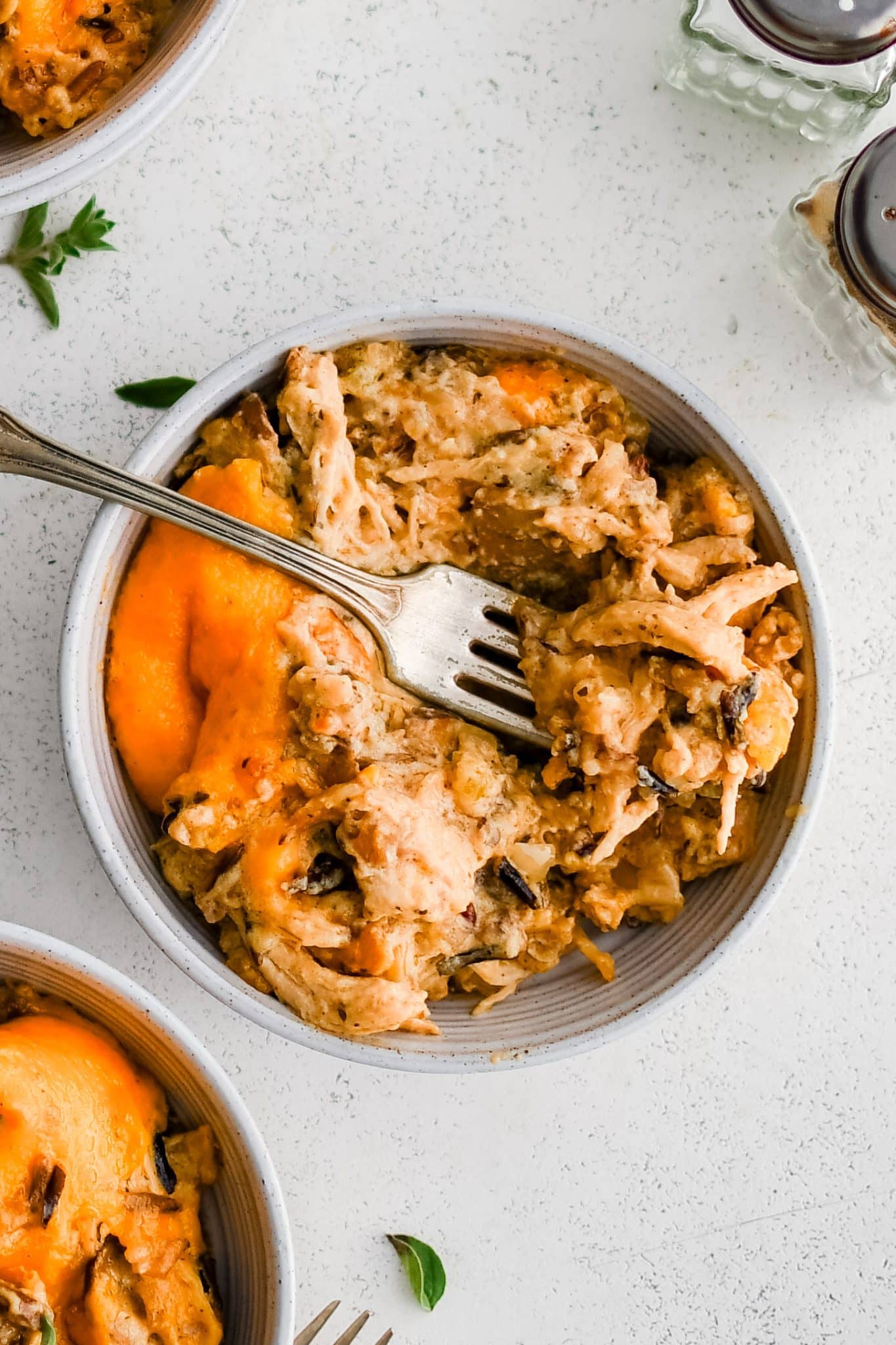 White serving bowl with a fork filled with a serving of messy chicken and wild rice casserole.