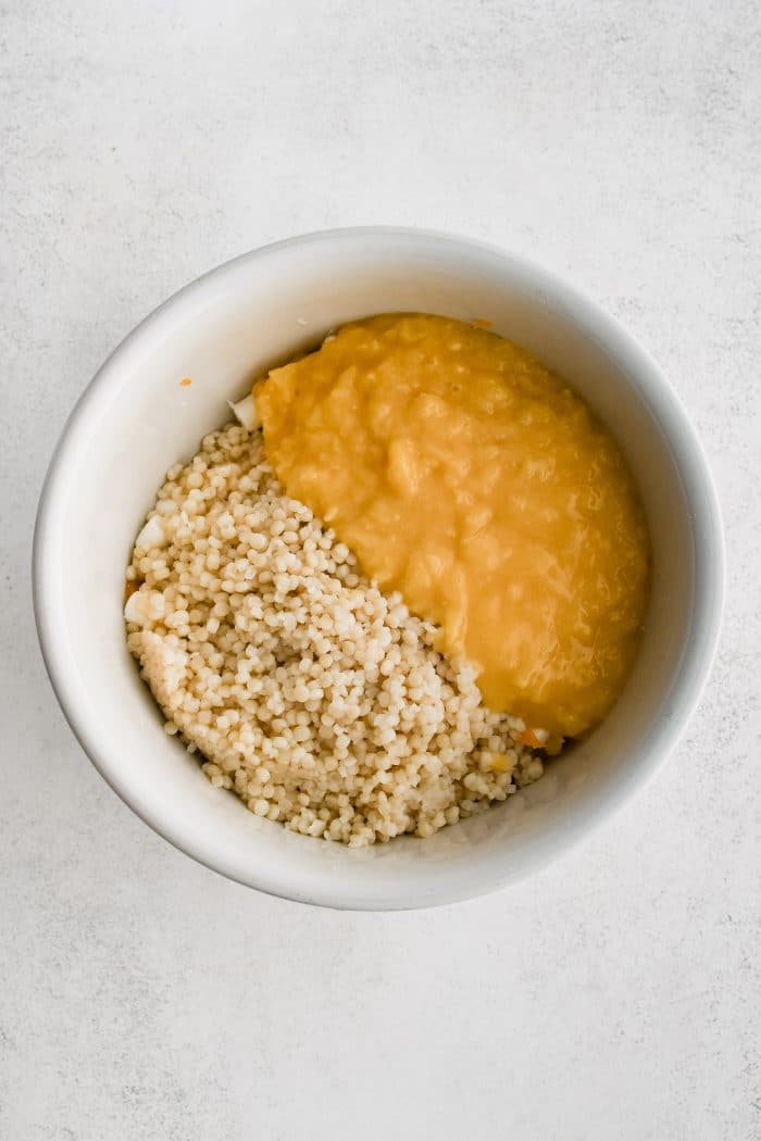 Cooled fruit sauce and cooked acini de pepe pasta added to the same white mixing bowl that is filled with tossed together pineapple tidbits, oranges, marshmallows, and coconut.