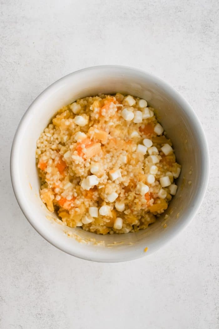 Large white bowl filled with tossed together pineapple tidbits, oranges, marshmallows, coconut, and cooked acini de pepe pasta mixed with cooled fruit sauce.