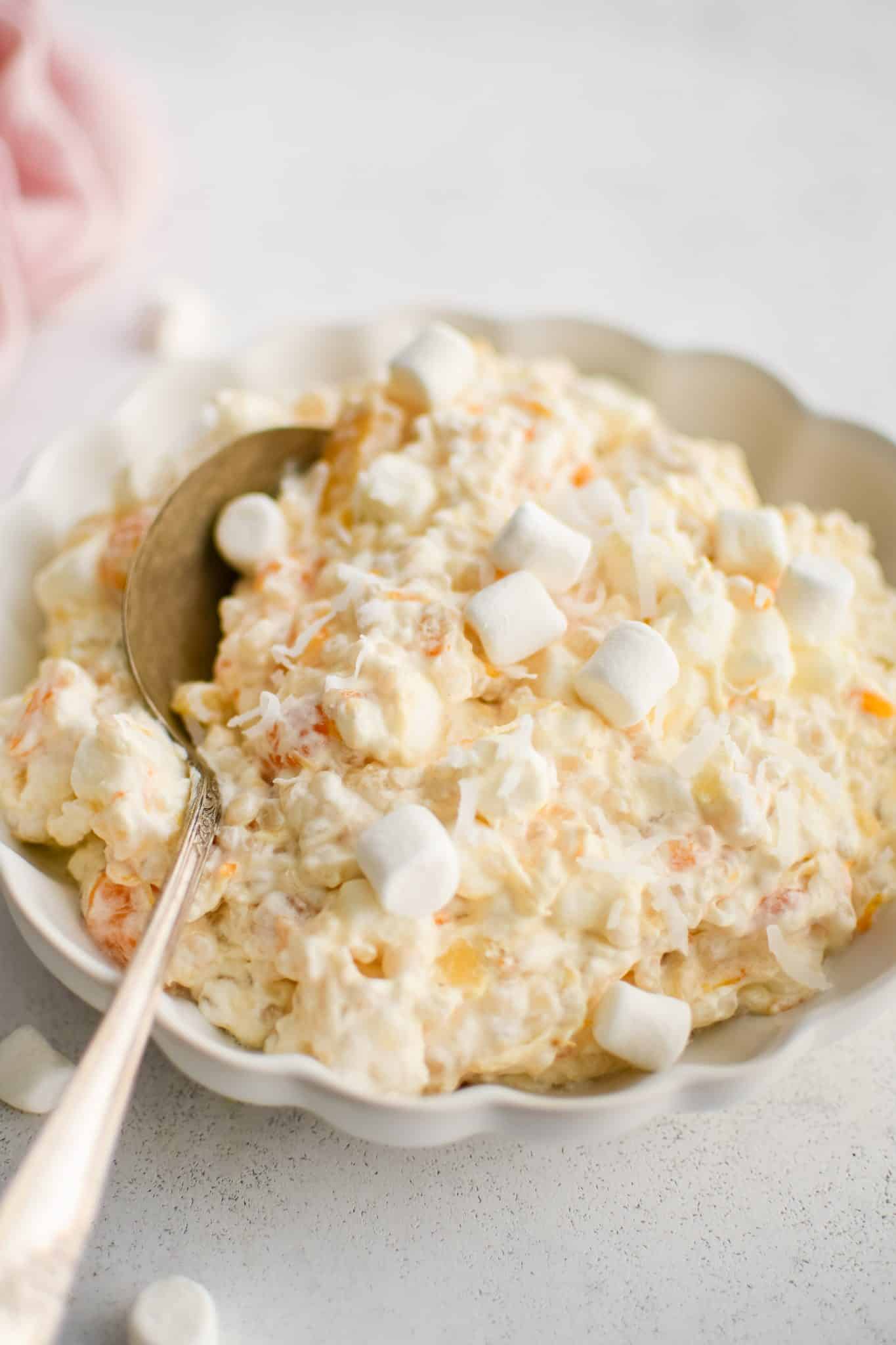 Scalloped edge serving bowl filled with creamy frog eye salad topped with additional mini marshmallows.