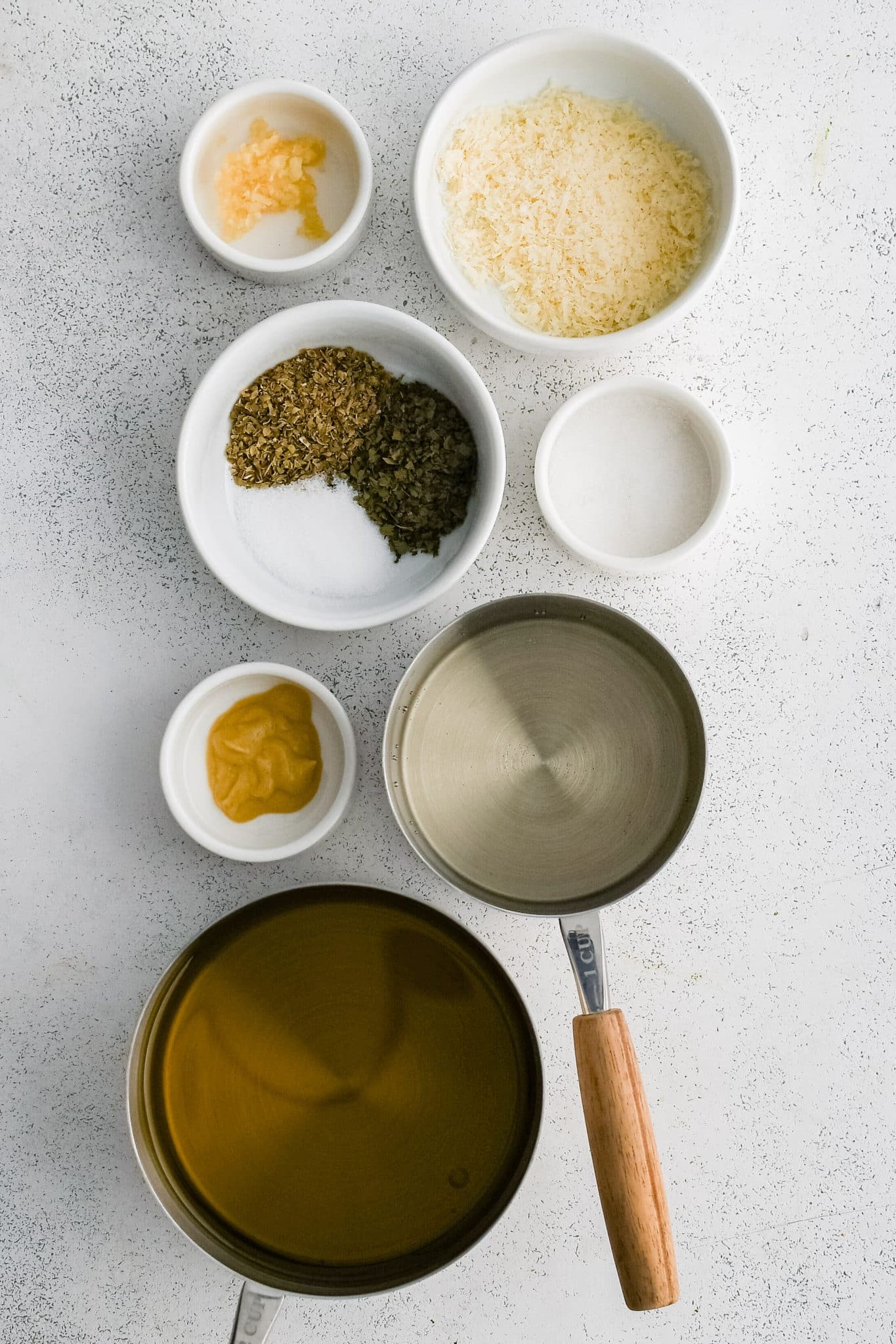 All of the ingredients for homemade Italian dressing presented in individual measuring cups and ramekins.