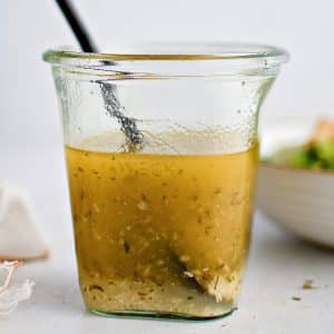 Glass jar filled with golden yellow Italian dressing that's been emulsified with the grated parmesan cheese settling on the bottom.