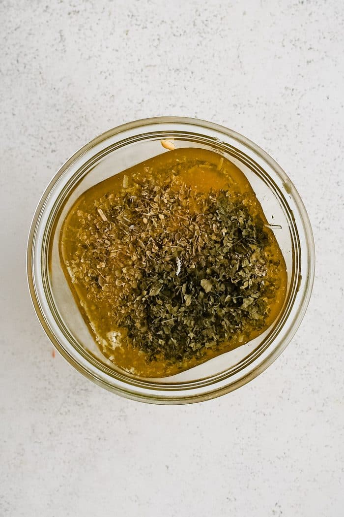 Glass mason jar filled with olive oil, white wine vinegar, grated parmesan, minced garlic, Dijon, dried oregano and parsley, salt, and sugar.