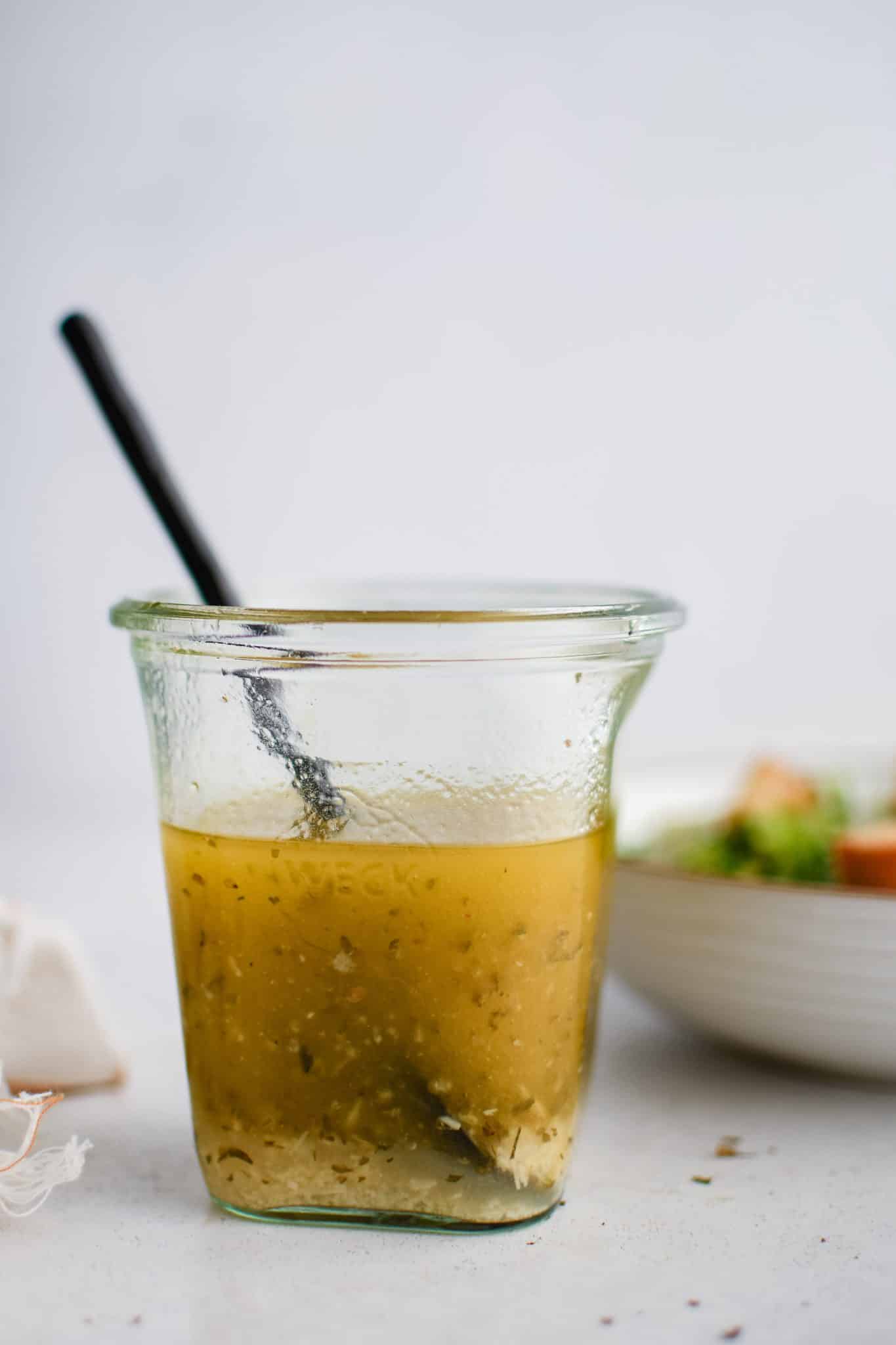 Glass jar filled with golden yellow Italian dressing that's been emulsified with the grated parmesan cheese settling on the bottom.