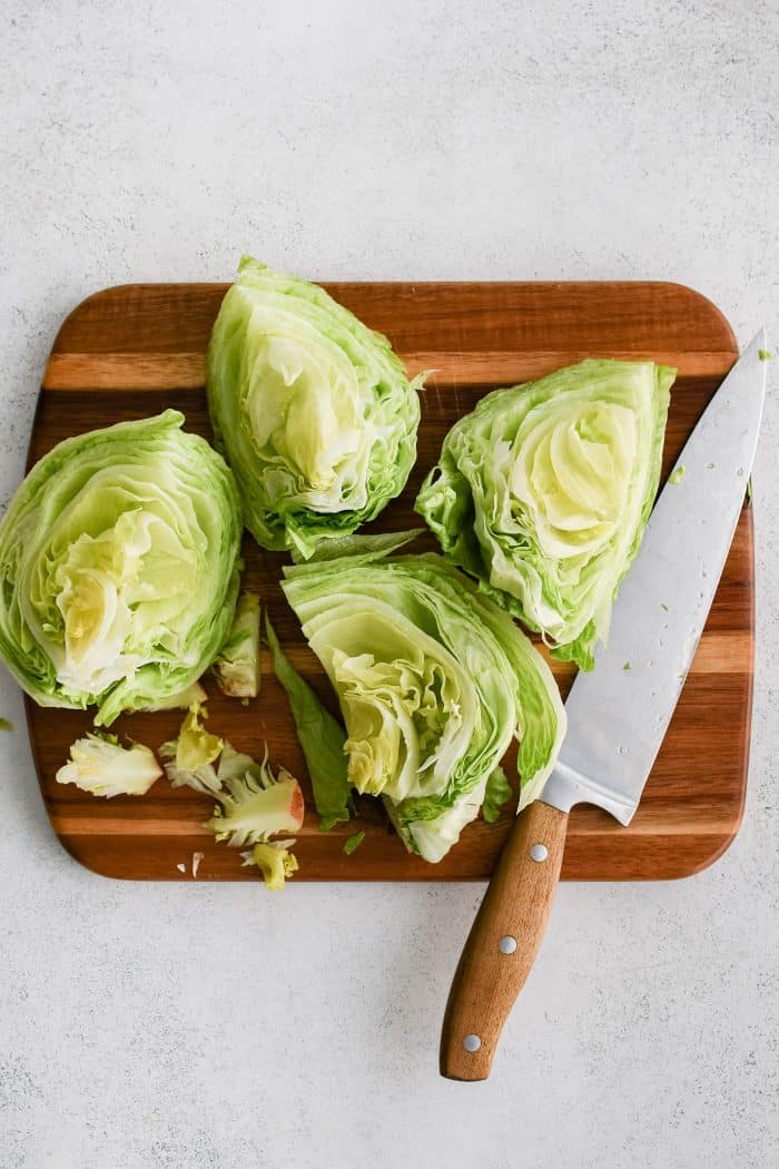 Four quarters of iceberg lettuce being trimmed on a large cutting board.