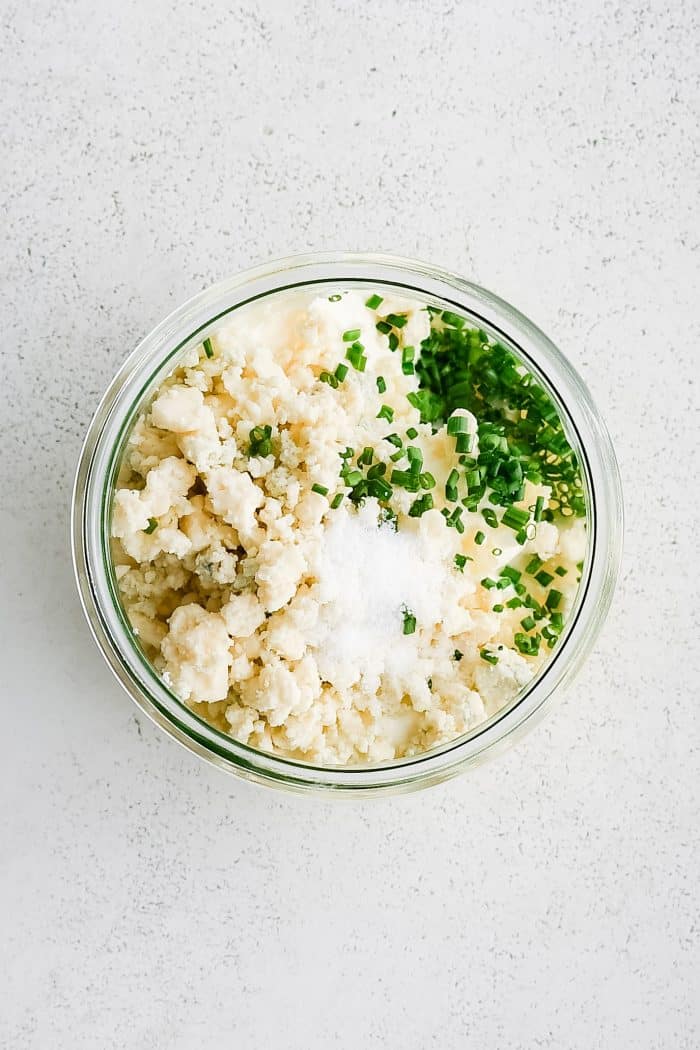 Small glass mixing bowl filled with sour cream, blue cheese, lemon juice, garlic, chives, and salt.