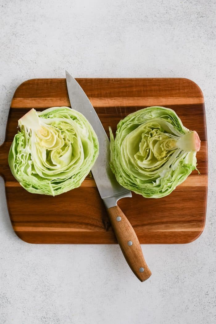 Large cutting board with two halves of an iceberg lettuce.