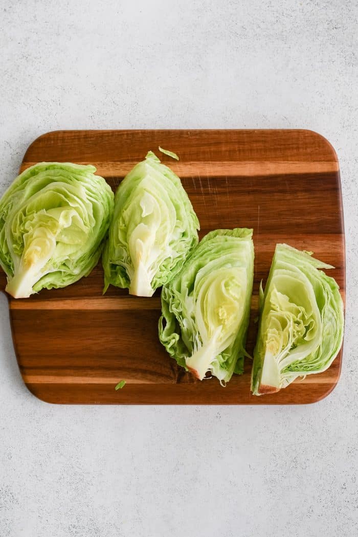 Large cutting board with one whole iceberg lettuce chopped into four quarters.