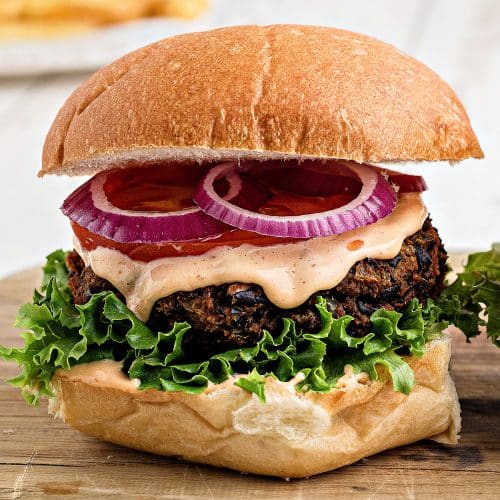 Assembled black bean burger with lettuce, chipotle mayo, sliced tomato, and and sliced red onion on a whole wheat bun.