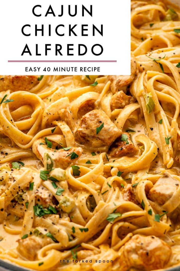 Vertical Pinterest pin for Cajun Chicken Alfredo featuring a close-up photo of creamy fettuccine Alfredo with browned chicken pieces, diced vegetables, chopped parsley, and black pepper. At the top is a large light gray text box with black capital letters reading CAJUN CHICKEN ALFREDO and smaller text below reading EASY 40 MINUTE RECIPE, separated by a mauve horizontal line. The words the forked spoon appear at the bottom.