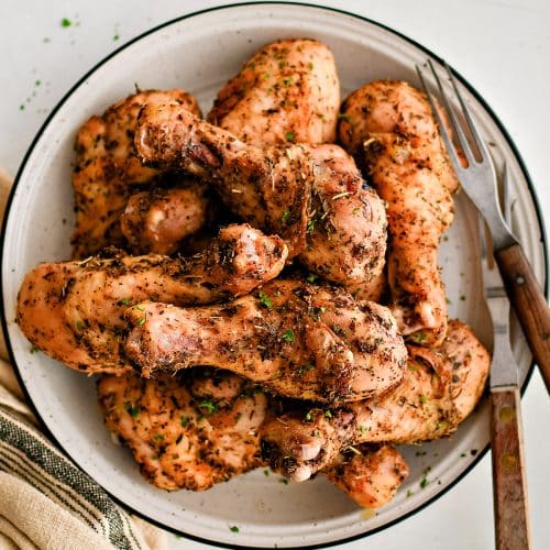 Round plate filled with crispy baked chicken leg drumsticks seasoned with dried herbs, garlic powder, onion powder, salt, and black pepper.