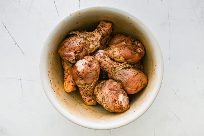 Raw chicken drumsticks fully coated in the seasoning mixture inside a large mixing bowl.