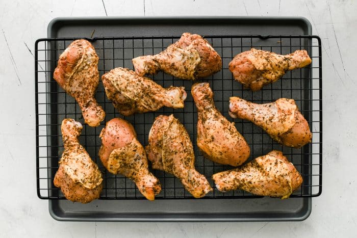 Seasoned chicken drumsticks spaced out on a wire rack set over a baking sheet, ready for the oven.