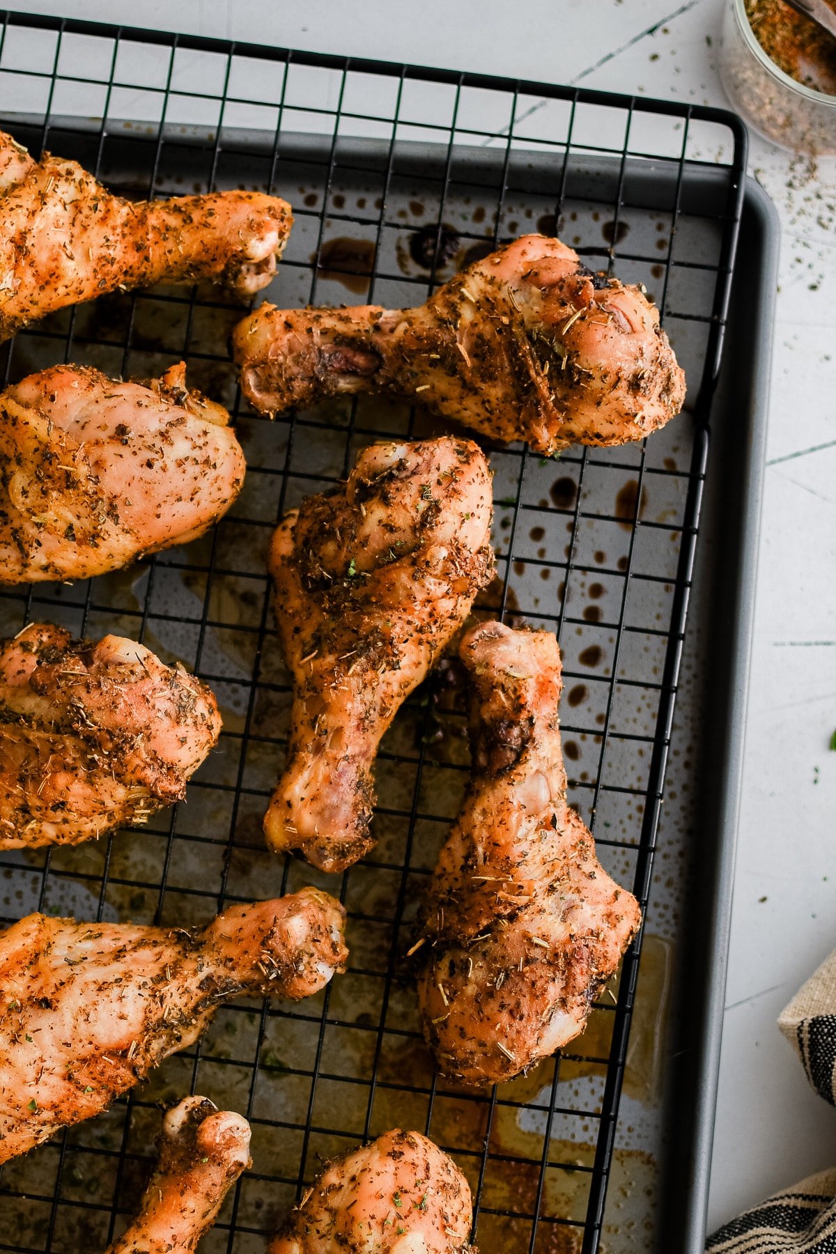Close-up of crispy baked chicken drumsticks resting on a wire rack with drippings underneath.