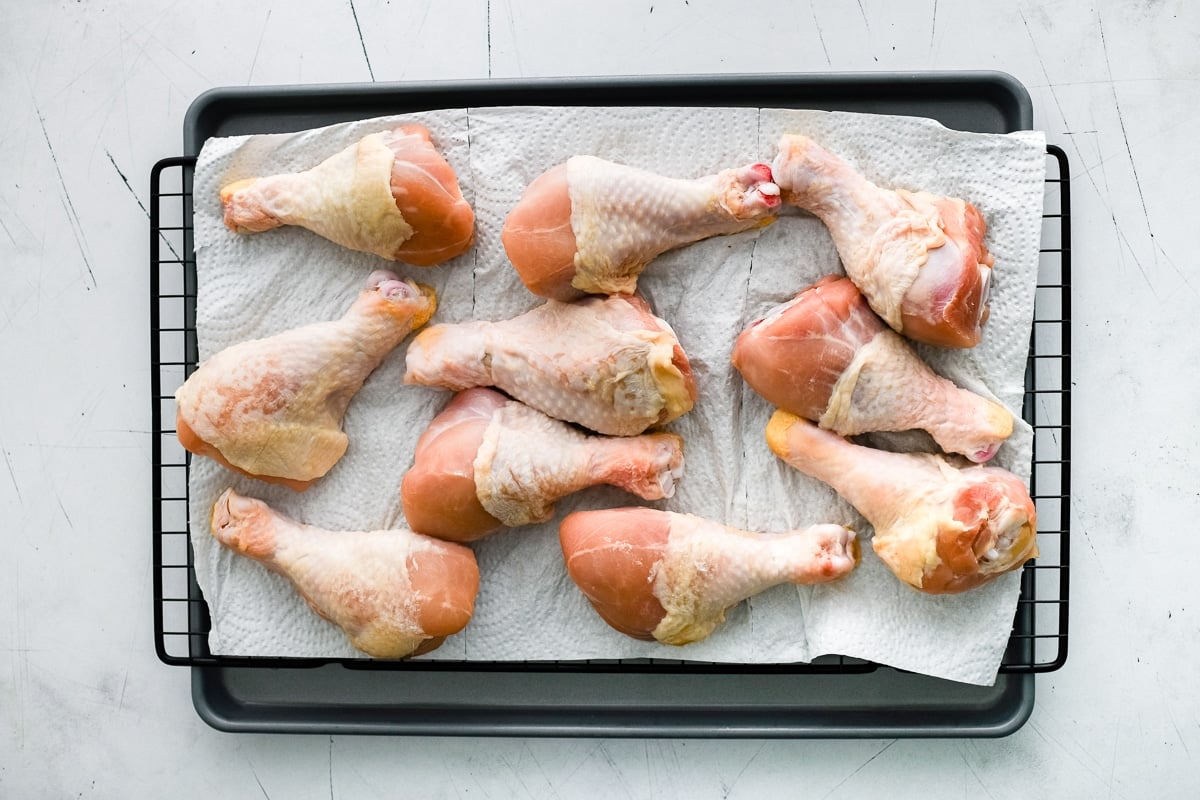 Raw chicken drumsticks laid out on a wire rack lined with paper towels to dry before seasoning.