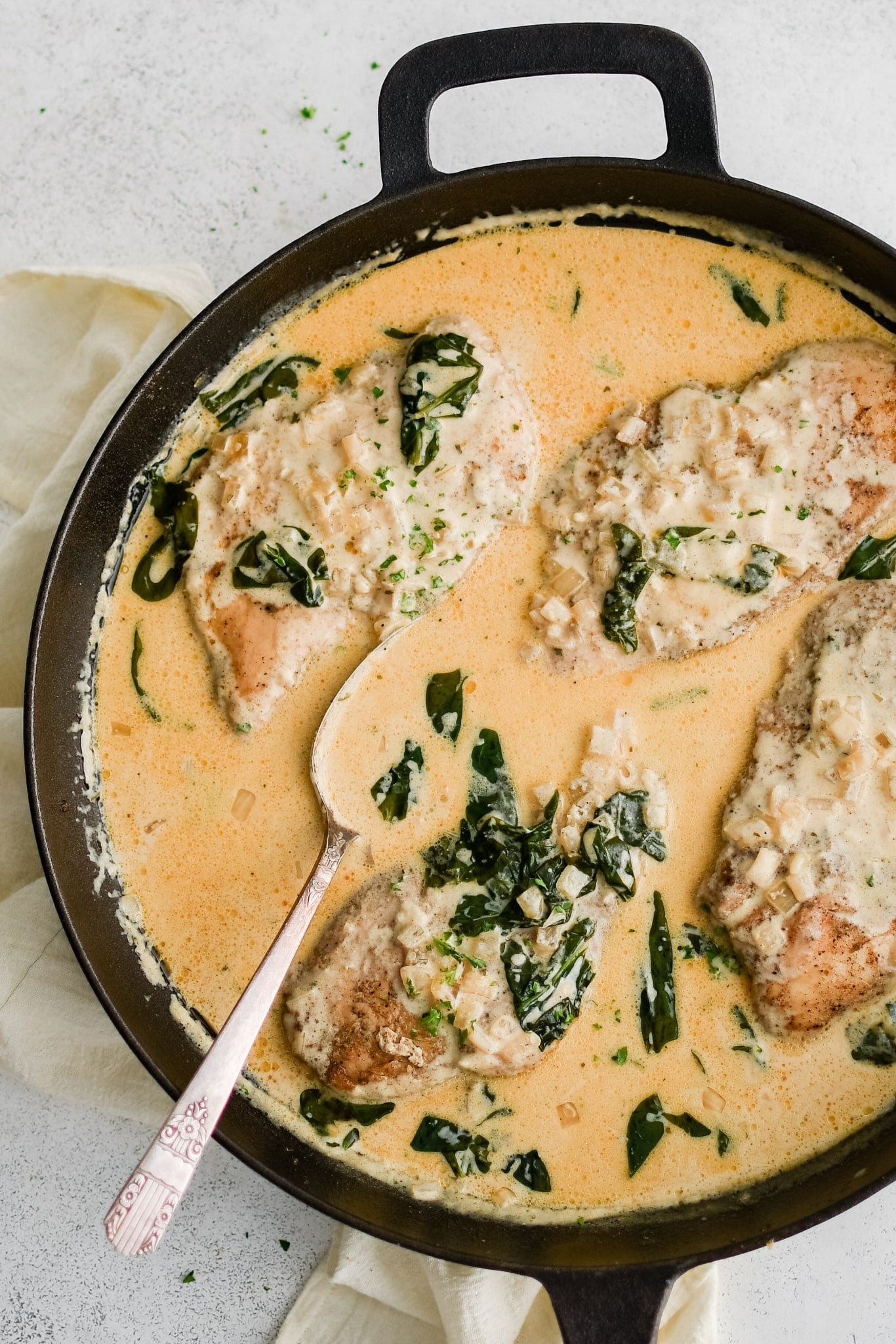 Well-seasoned and cooked chicken cutlets nestled into a large cast-iron skillet filled with simmering boursin cheese sauce with spinach and onions.