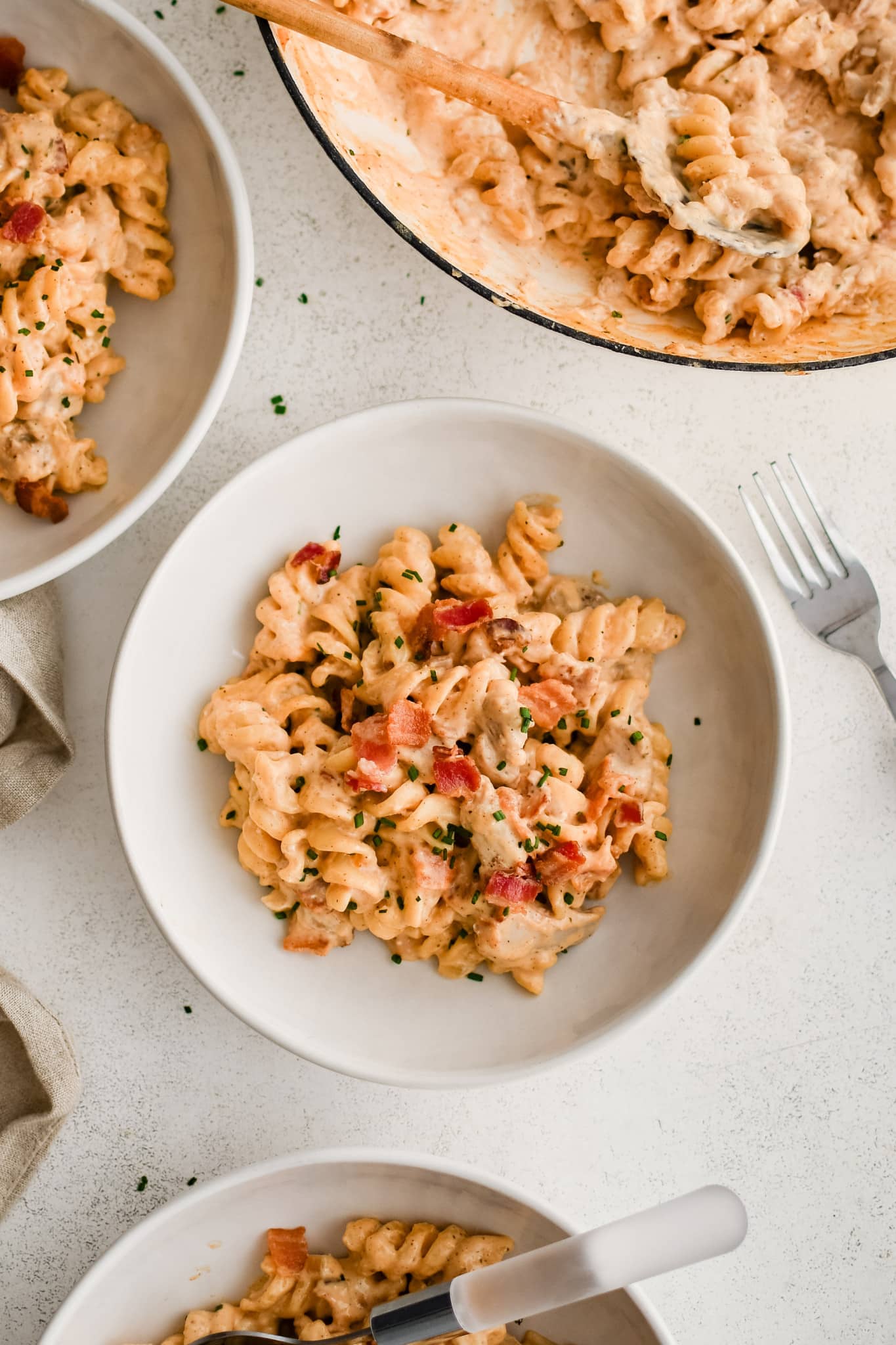 White shallow pasta bowl filled with bacon ranch pasta salad topped with crispy bacon pieces and diced chives.
