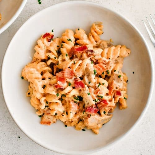 White shallow pasta bowl filled with bacon ranch pasta salad topped with crispy bacon pieces and diced chives.