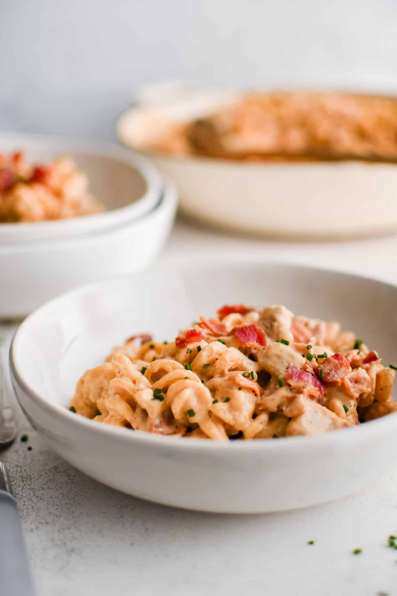 White shallow pasta bowl filled with bacon ranch pasta salad topped with crispy bacon pieces and diced chives.