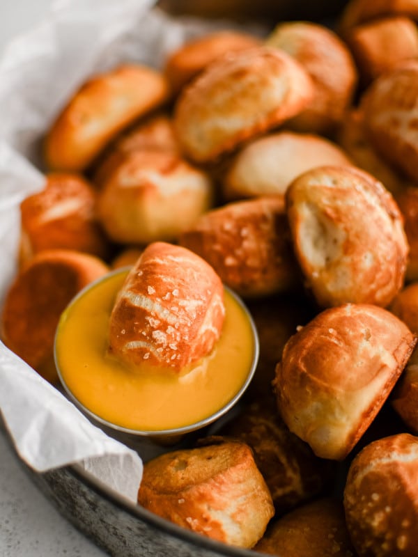 Dozens of soft pretzel bites topped with coarse sea salt and served with a side of beer cheese served in a large aluminum serving tray.