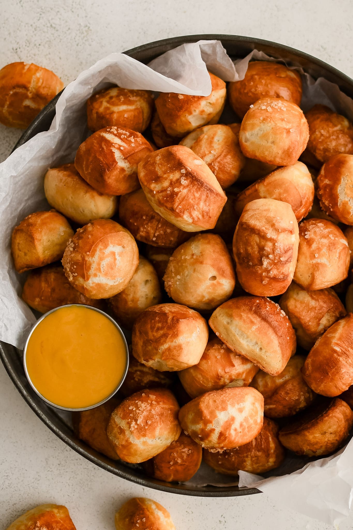 Dozens of soft pretzel bites topped with coarse sea salt and served with a side of beer cheese served in a large aluminum serving tray.