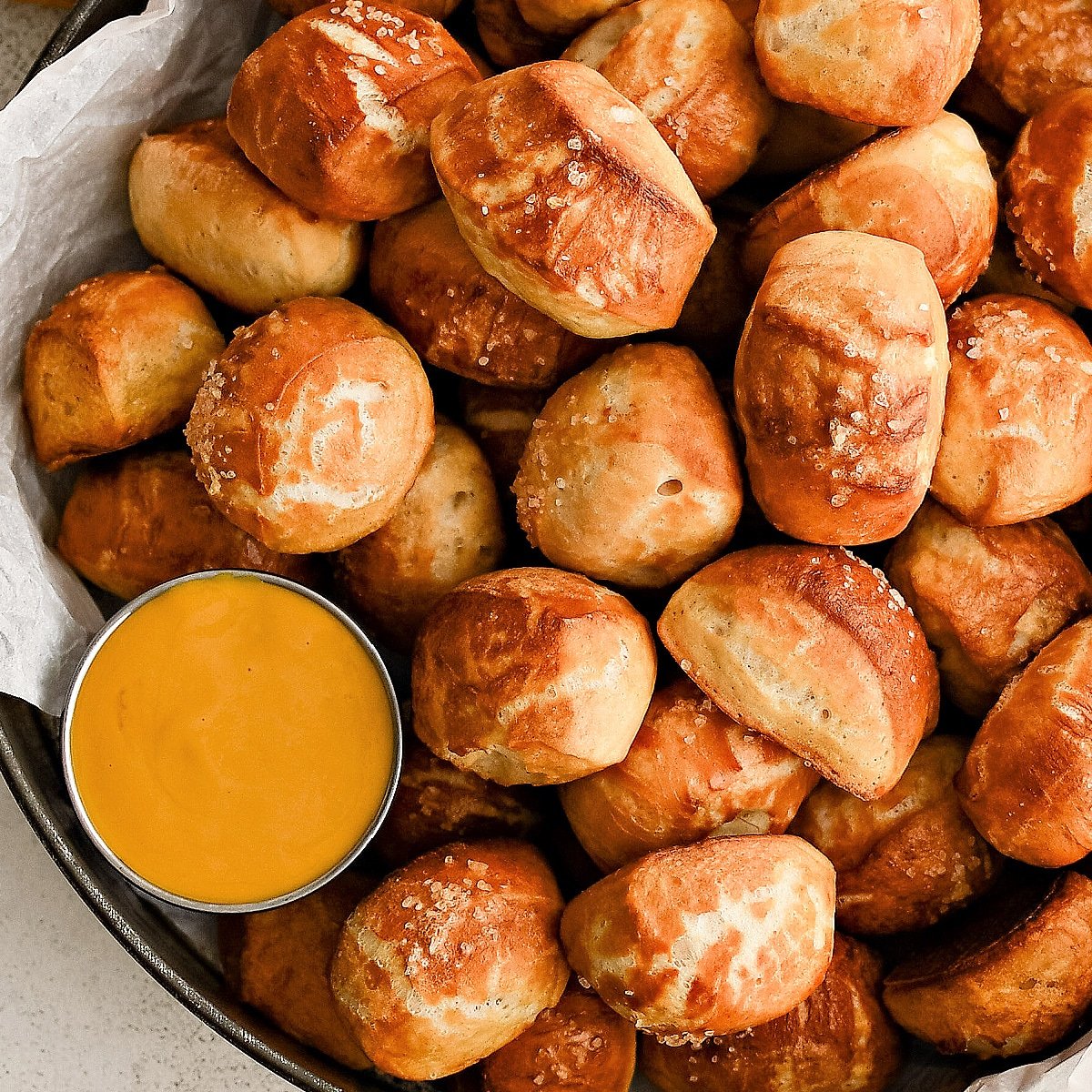 Dozens of soft pretzel bites topped with coarse sea salt and served with a side of beer cheese served in a large aluminum serving tray.