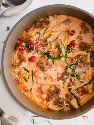 Large soup pot filled with cooked Italian sausage soup garnished with fresh basil.