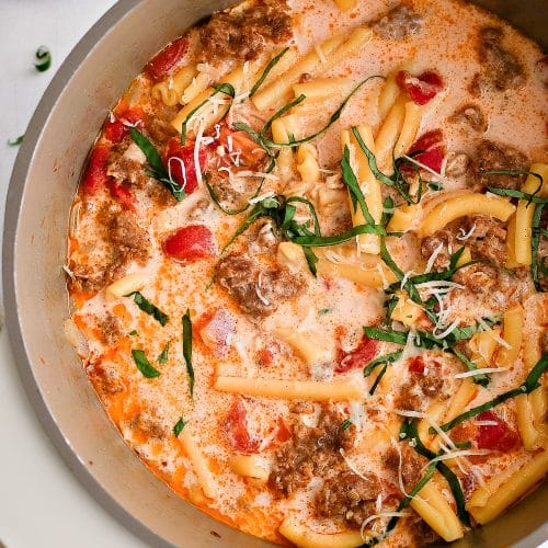 Large soup pot filled with cooked Italian sausage soup garnished with fresh basil.