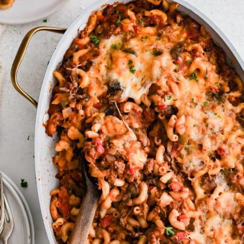 Large wooden serving spoon settled into a large casserole pan filled with hot and cheese Johnny Marzetti casserole.