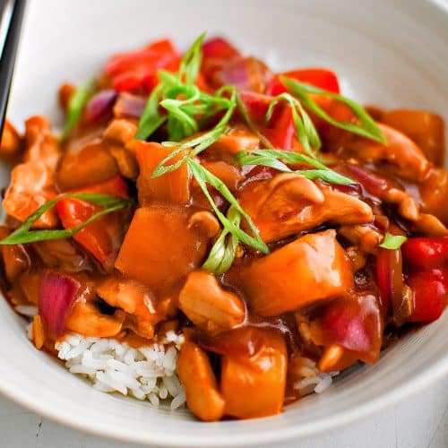 White serving bowl filled with cooked white rice and topped with pineapple chicken coated in a sticky, sweet, and savory pineapple stir-fry sauce and garnished with fresh green onions.