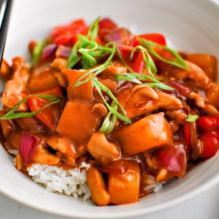 White serving bowl filled with cooked white rice and topped with pineapple chicken coated in a sticky, sweet, and savory pineapple stir-fry sauce and garnished with fresh green onions.